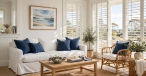 Bright Hamptons style living room with white linen sofa, navy cushions and rattan chair