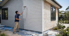 Professional painter rolling fresh paint onto the weatherboard exterior of an Australian home