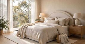 Bright styled master bedroom with upholstered bed, bedside tables, lamps and sheer-curtained windows