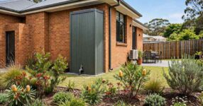 Slimline rainwater tank in woodland grey steel installed beside a brick Australian home with native garden