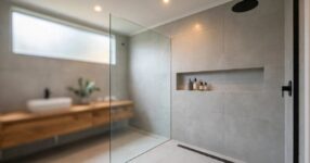 Modern Australian bathroom walk-in shower with frameless glass screen, large-format grey porcelain tiles, linear drain and matte black rain showerhead